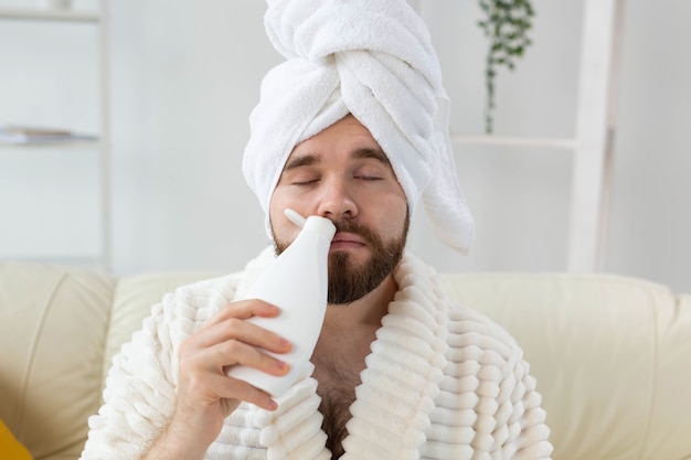 Homme barbu avec une serviette sur la tête en appliquant une crème pour le corps guy sourire quand l'odeur de la crème lotion sur