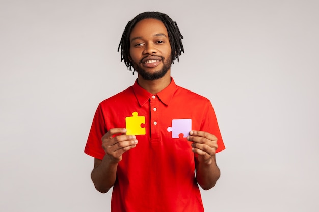 Homme barbu souriant et calme tenant des pièces de puzzle jaunes et violettes, résolvant des problèmes et des tâches.