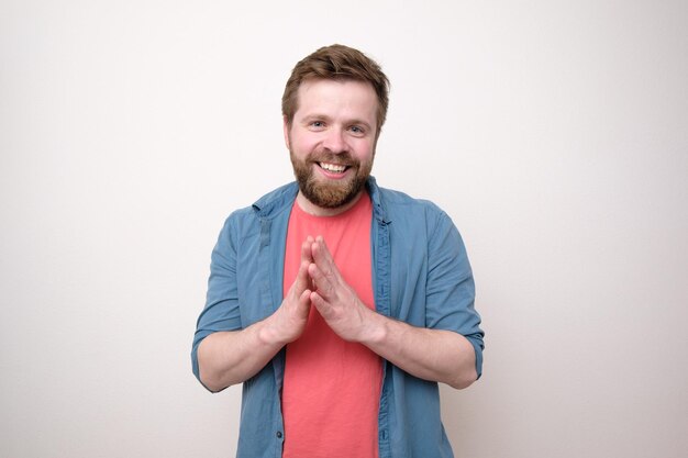 Homme barbu souriant calmement et en toute confiance regardant la caméra avec les paumes ensemble