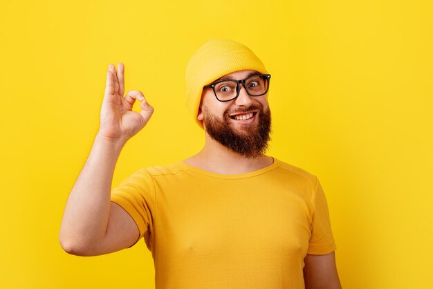 Homme barbu souriant dans des verres montrant un geste ok sur fond jaune