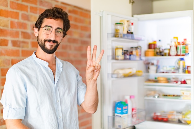 Homme barbu souriant et à la sympathique, montrant le numéro trois ou troisième avec la main en avant, compte à rebours