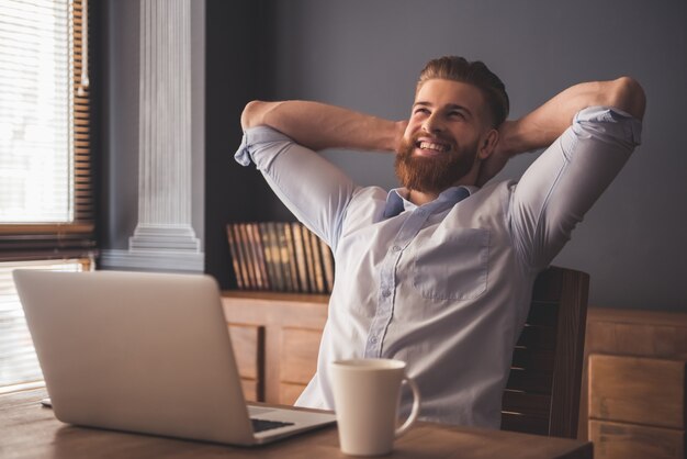 Homme barbu sourit en se relaxant sur une chaise dans le bureau