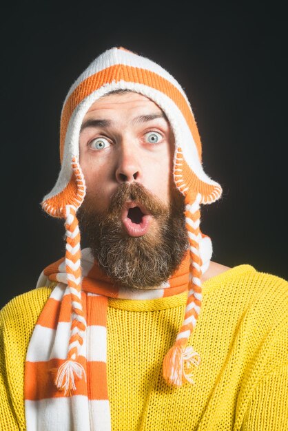 Homme barbu surpris en écharpe à chapeau drôle rayé et pull jaune bel homme barbu étonné