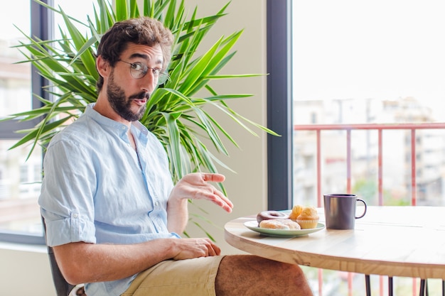 Homme barbu à la surprise et choqué, avec la mâchoire tombée tenant un objet avec une main ouverte sur le côté