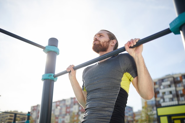 Homme barbu suspendu à un bar en plein air