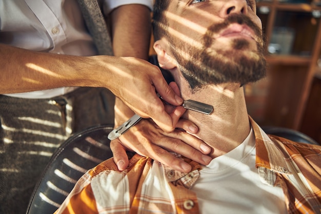 homme barbu tenant la tête haute pour qu'un coiffeur le rase