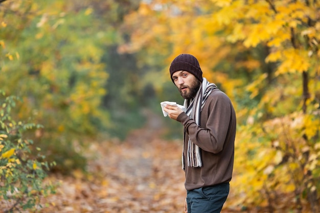 Homme barbu triste et malade avec une écharpe à la main à l'automne dans la forêt