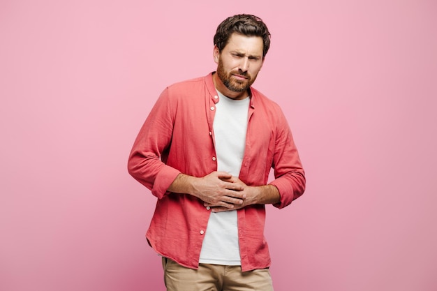 Un homme barbu triste avec des problèmes de santé, des maux d'estomac posant sur un fond rose.