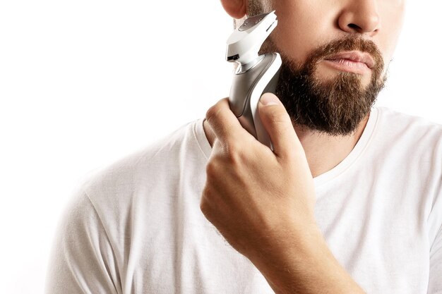 L'homme barbu utilise une tondeuse électrique sur fond blanc