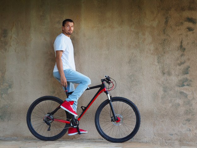 Homme barbu vêtu d'un jean et d'une sneaker rouge sur un vélo