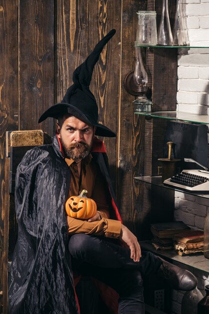 Homme barbu avec un visage d'horreur tenant une lanterne de citrouille à tête de citrouille sur fond de bois. Halloween de vacances avec des costumes de carnaval drôles sur fond de vacances.