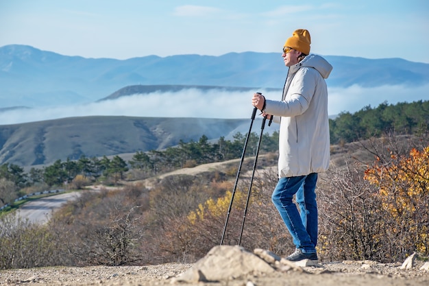 Un homme avec des bâtons de marche nordique se dresse dans les montagnes et regarde devant lui