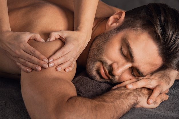 Un homme beau se faire un massage du dos couché au spa, main de femme faisant signe coeur amour concept