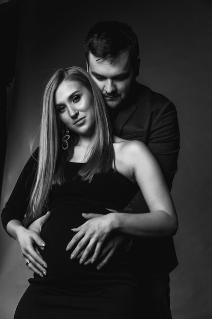 Un homme et une belle femme enceinte se tiennent sur le fond du mur de la pièce. Photo noir et blanc