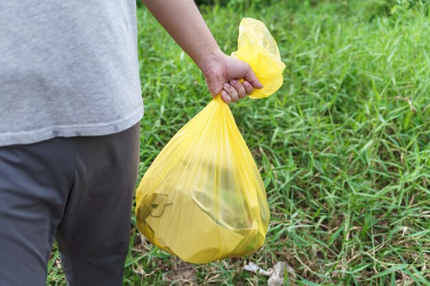 Photo homme bénévole caritatif tenant un sac jaune à ordures et des ordures de bouteilles en plastique pour le nettoyage du recyclage