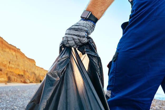 Homme bénévole debout sur la plage avec un sac plein de déchets collectés