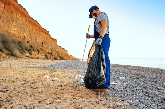 Un homme bénévole ramassant des ordures sur la plage avec un bâton d'extension de portée