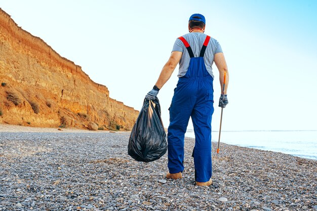 Homme bénévole à l'Uniforn la collecte des ordures sur la plage avec un bâton d'extension de portée