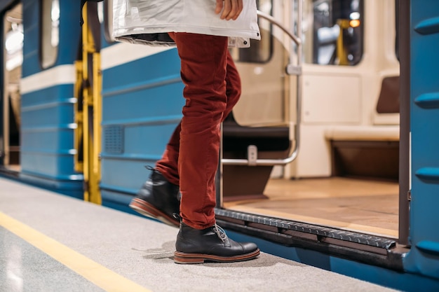 Un homme bien habillé en chaussures noires, pantalon rouge et veste blanche entre dans une rame de métro