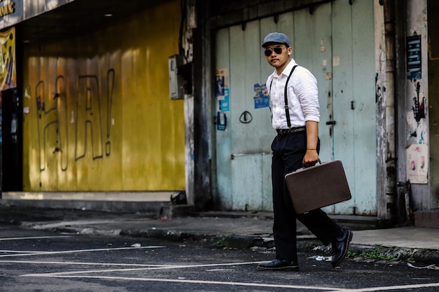 Un homme bien habillé porte une valise vintage dans la rue