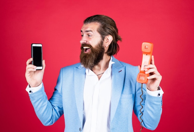 Un homme bien soigné en tenue de soirée de mariage a la barbe utilise un téléphone rétro et la technologie moderne des smartphones