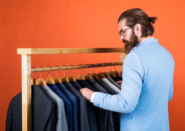 Un homme bien soigné en tenues de soirée de mariage a une barbe choisir une veste dans un designer de garde-robe