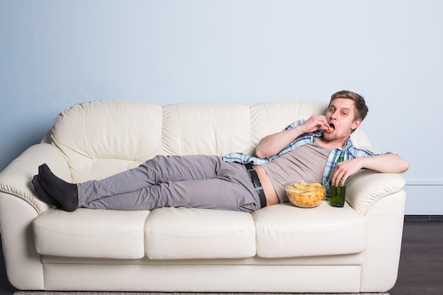 Homme avec de la bière et des frites devant la télévision à la maison.