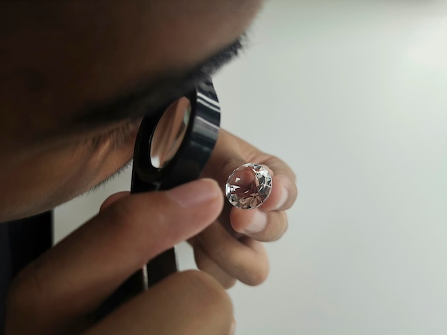 L'homme bijoutier examine le diamant poli à travers la loupe L'acheteur vérifie le diamant Diamant taillé et poli