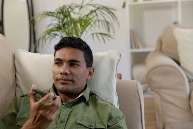 Un homme biracial heureux allongé sur le canapé en utilisant un smartphone à la maison