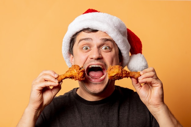 Homme blanc au chapeau de Noël avec des pilons de poulet sur un mur blanc