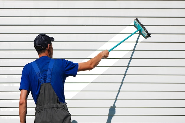 L'homme blanc en salopette lave le mur avec une brosse