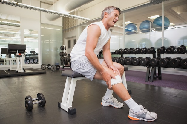 Homme blessé agrippant son genou dans la salle de musculation