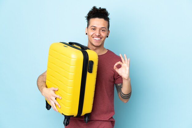 Homme sur bleu isolé en vacances avec valise de voyage et faire signe OK