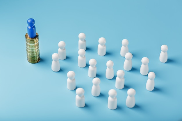 Photo l'homme bleu se tient sur des pièces d'or en argent et contrôle une foule de blancs. le concept de pouvoir gourmand et de gestion des personnes.