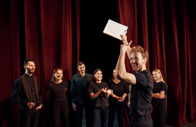 Un homme avec un bloc-notes pratique son rôle Un groupe d'acteurs en vêtements de couleur foncée à la répétition au théâtre