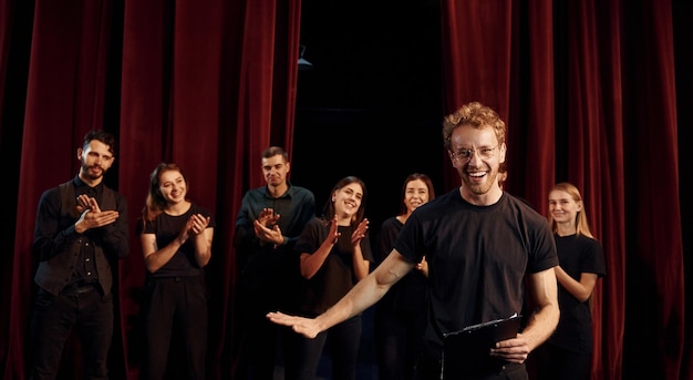 Un homme avec un bloc-notes pratique son rôle Un groupe d'acteurs en vêtements de couleur foncée à la répétition au théâtre