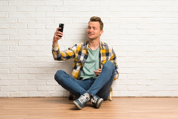 Homme blond assis sur le sol faisant un selfie