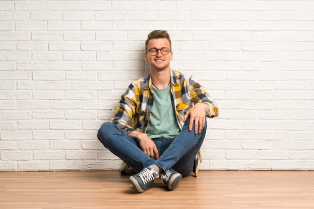 Homme blond assis sur le sol avec des lunettes et heureux