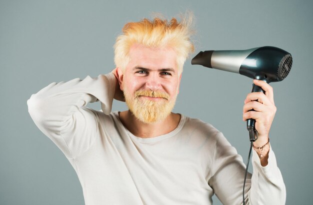 Un homme blond barbu aux cheveux secs, un homme beau aux cheveux longs se sèche les cheveux avec un sèche-cheveux.