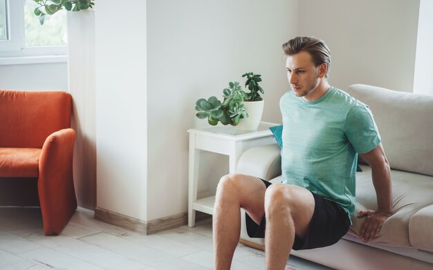 Homme blond caucasien s'entraîne à la maison sans équipement portant des vêtements de sport pendant les exercices de fitness