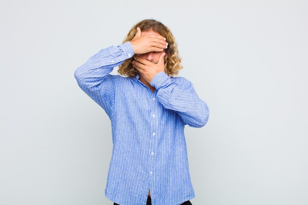 Homme blond couvrant le visage avec les deux mains