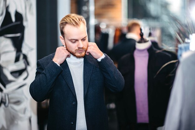 Un homme blond du millénaire en tenue d'affaires choisit des vêtements dans un magasin L'homme fait du shopping