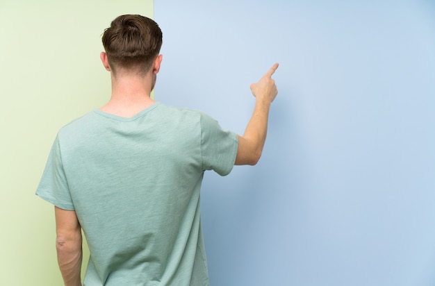 Homme blond sur un mur blanc isolé, gardant une conversation avec le téléphone portable