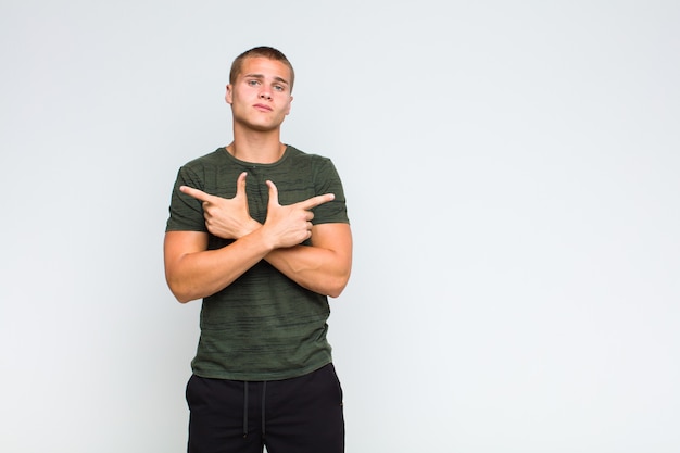 Homme blond à la perplexité et confus et pointant dans des directions opposées avec des doutes