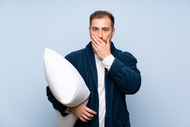 Homme blond en pyjama sur un mur bleu avec une expression faciale surprise