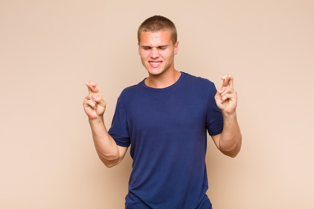 Homme blond souriant et croisant anxieusement les deux doigts, se sentant inquiet et souhaitant ou espérant avoir de la chance