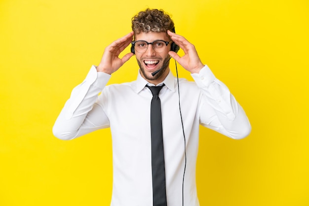 Homme blond télévendeur travaillant avec un casque isolé sur fond jaune avec une expression de surprise