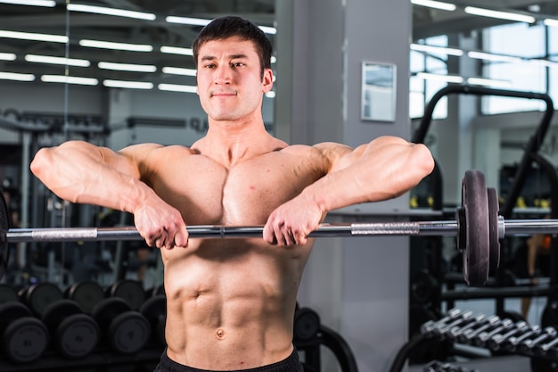 Homme bodybuilder avec biceps, triceps et poitrine parfaits dans la salle de gym