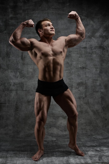 Homme bodybuilder sexy posant en pleine croissance sur fond sombre en short noir. Beau corps masculin pompé isolé avec espace libre pour la publicité