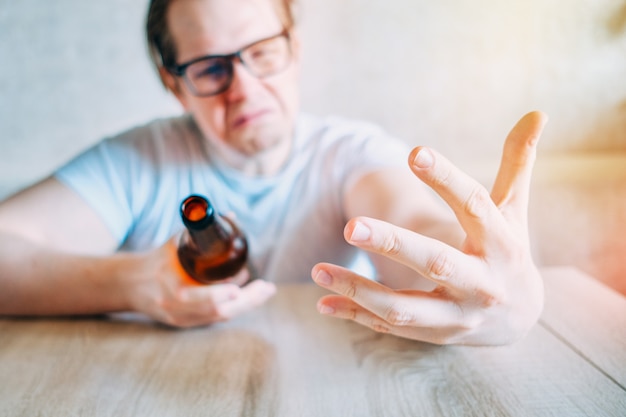 Un homme boit de l'alcool à la maison et jure de façon abstraite.